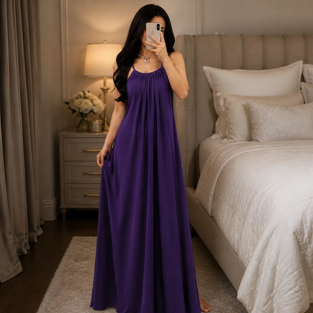 Model wearing a black backless maxi dress and silky lounge gown by Soft Secrets in a luxury bedroom setting.